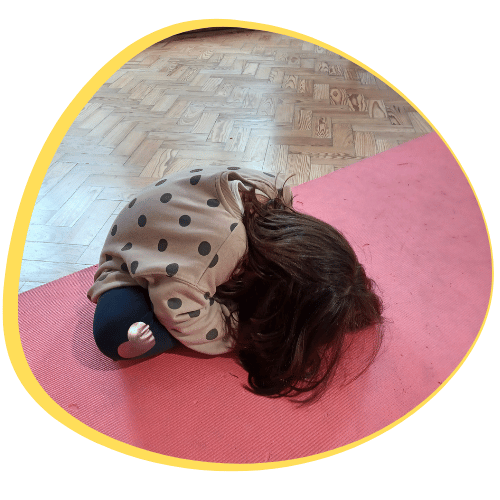 Criança na postura de yoga da tartaruga, numa sessão de Histórias que se Mexem, integrando leitura e movimento.